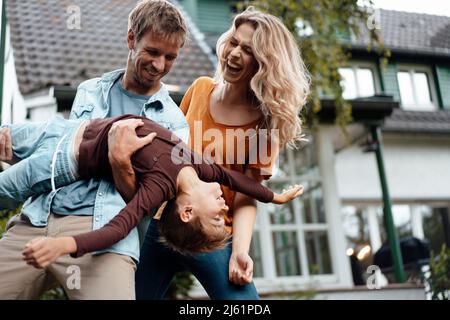 Verspielter Mann trägt Sohn von fröhlichen Frau genießen im Hinterhof Stockfoto