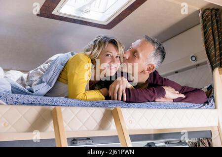 Mann küsst Frau auf dem Bett im Wohnmobil liegend Stockfoto