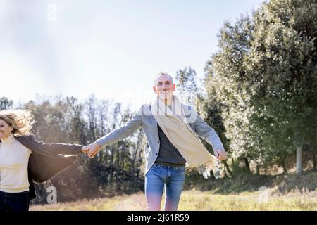 Glückliches reifes Paar, das die Hände hält und auf grasbewachsenem Land läuft Stockfoto