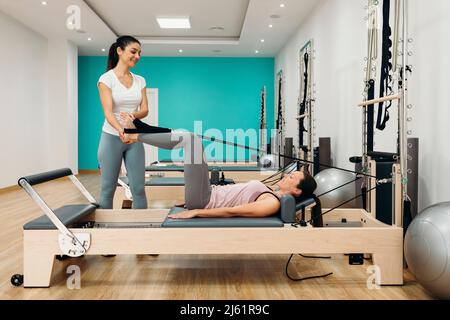 Lächelnder Fitnesstrainer unterstützt Frau bei Pilates im Studio Stockfoto