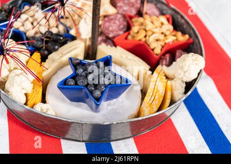 Am 4. Juli gab es ein Charcuterie-Brett auf einem zweistufigen Metallständer, gefüllt mit Käse, Crackern, Salami und frischem Obst Stockfoto