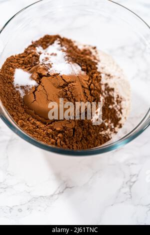 Mischen Sie trockene Zutaten in einer großen Glasmischschüssel, um Schokoladenkekse mit Schokoladenherzen zum Valentinstag zu backen. Stockfoto