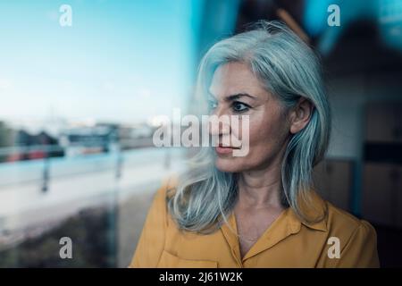 Nachdenkliche Geschäftsfrau mit grauem Haar, das durch Glas gesehen wird Stockfoto