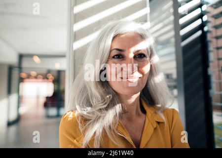 Lächelnde Frau, die vor der Säule am Arbeitsplatz steht Stockfoto