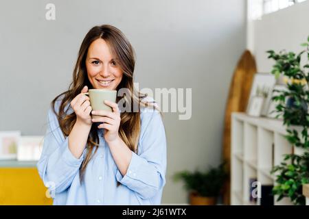 Lächelnde schöne Frau mit Kaffeetasse zu Hause Stockfoto