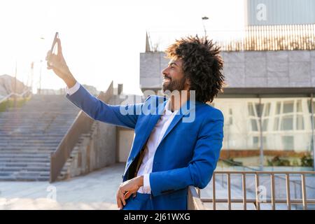 Glücklicher Geschäftsmann, der Selfie über das Mobiltelefon nimmt und sich auf das Geländer stützt Stockfoto