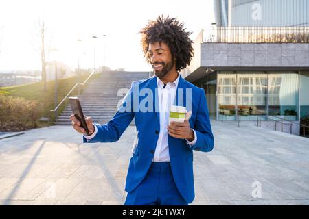Lächelnder Geschäftsmann hält einen Einweg-Becher, der Selfie über das Mobiltelefon auf dem Weg hält Stockfoto