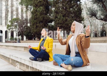 Geschäftsfrauen sitzen mit gekreuzten Beinen und meditieren auf Stufen Stockfoto