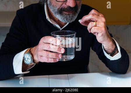 Älterer Mann mit einem Glas Wasser am Tisch Stockfoto