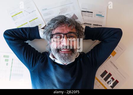 Lächelnder Freiberufler mit Händen hinter dem Kopf, der zu Hause auf Dokumenten liegt Stockfoto
