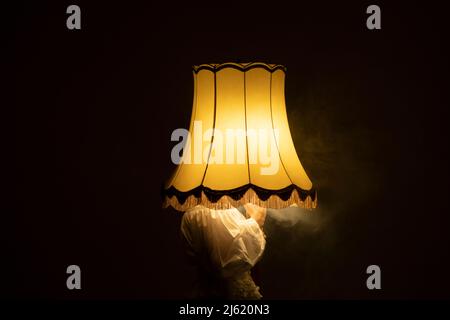 Junge Frau, die im dunklen Raum das Gesicht mit einer rauchig beleuchteten Lampe bedeckt Stockfoto