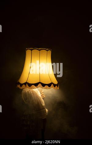 Junge Frau versteckt Gesicht mit rauchig beleuchteten Lampe in dunklen Raum Stockfoto