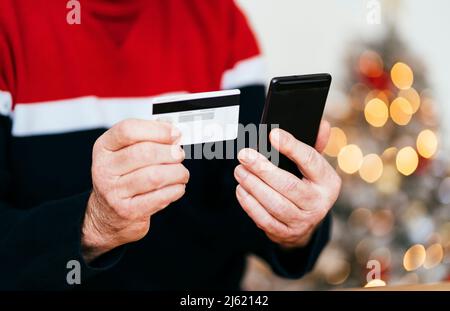 Hand eines älteren Mannes mit Kreditkarte und Mobiltelefon zu Hause Stockfoto