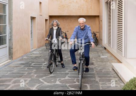 Lächelndes Seniorenpaar, das auf dem Fußweg Fahrrad fährt Stockfoto
