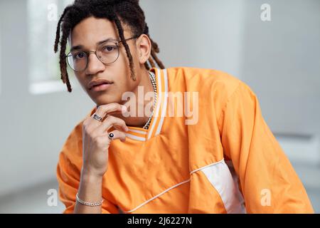 Junger Mann mit der Hand am Kinn und einer Brille Stockfoto