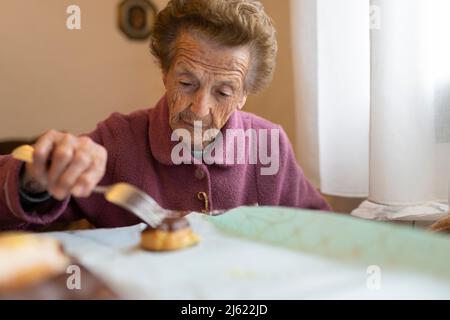 Ältere Frau mit Cupcake sitzt am Esstisch Stockfoto