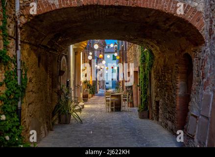 Italien, Provinz Siena, Radicondoli, Lanterns beleuchtete Altstadtallee mit Backsteinbogen im Vordergrund Stockfoto