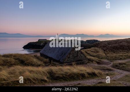 Großbritannien, Wales, Newborough, Küstenhütte auf Ynys Llanddwyn bei Sonnenuntergang mit Twr Mawr Leuchtturm im Hintergrund Stockfoto