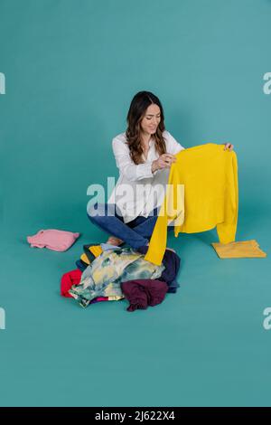 Lächelnde Frau mit gelbem Pullover und Kleidung vor blauem Hintergrund Stockfoto