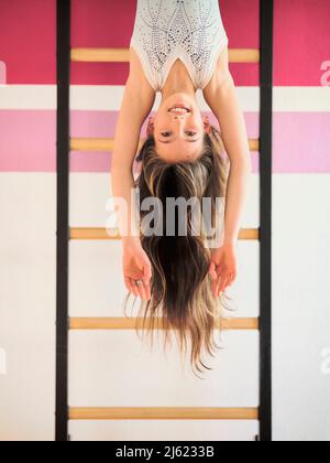 Lächelndes Mädchen, das kopfüber an den Wandstangen hängt Stockfoto