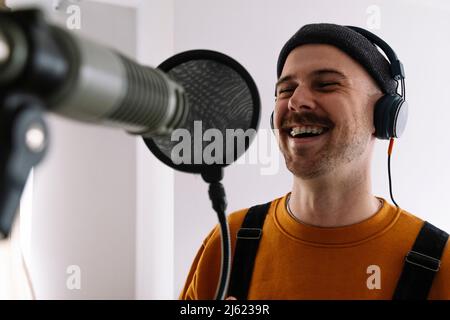 Fröhlicher Freiberufler mit Mikrofon, der im Heimstudio singt Stockfoto