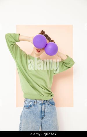 Frau, die die Augen mit lila Ballons bedeckt, die vor weißem Hintergrund stehen Stockfoto