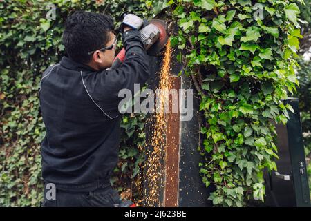 Mann, der eine Mühle benutzt, die am Metalltor arbeitet Stockfoto