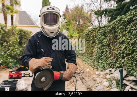 Mann mit Schweißhelm, der mit Grinder auf der Baustelle steht Stockfoto