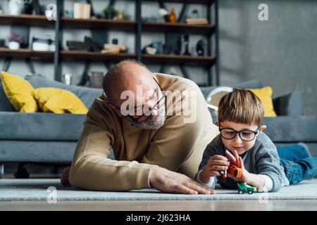 Älterer Mann, der Enkel beim Spielen mit einem Spielzeugauto im Wohnzimmer ansieht Stockfoto