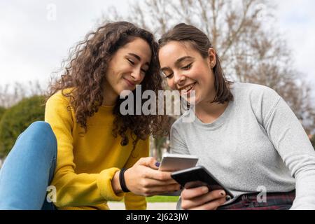 Glückliche Freunde, die im Park Smartphones nutzen Stockfoto
