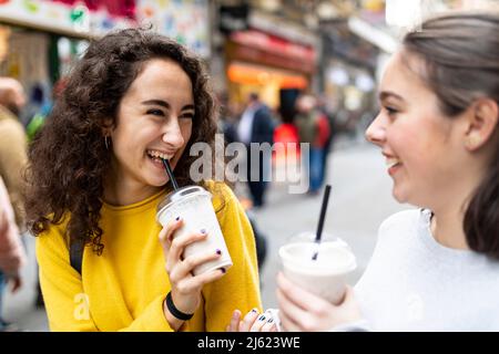 Glückliche junge Frau, die einen Freund beim Milchshake ansieht Stockfoto
