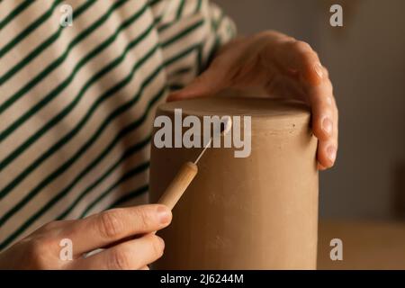 Hände einer Frau, die Ton mit einem Handwerkzeug in der Werkstatt formt Stockfoto