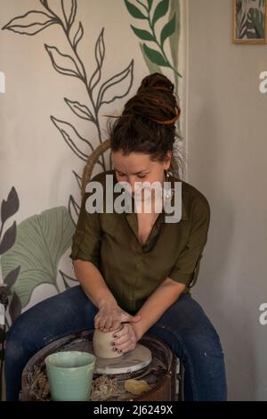 Glückliche Frau, die Tontopf auf Töpferscheibe in der Werkstatt macht Stockfoto