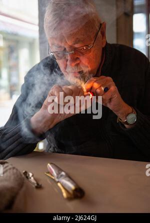 Ein älterer Mann mit Brillen raucht Zigarre und sitzt am Tisch Stockfoto