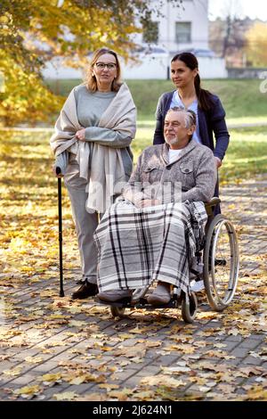 Ältere Frau im Gespräch mit Krankenschwester und einem behinderten Mann, der im Rollstuhl im Park sitzt Stockfoto
