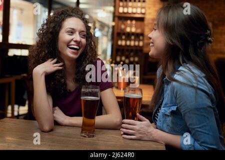 Zwei glückliche Freundinnen, die in einem Pub Bier trinken und sich unterhalten Stockfoto