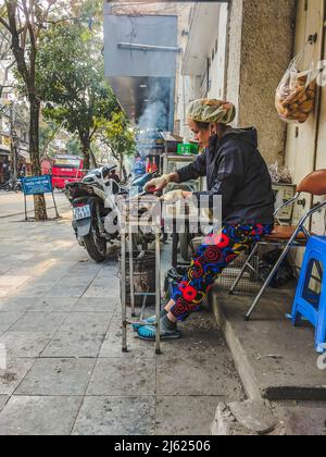 Eine Frau kocht Straßenessen auf dem Fußweg in Hanoi, Vietnam Stockfoto