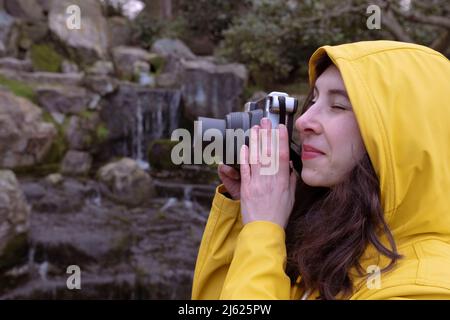 Junge Frau, die durch die Kamera schaut und im Wald fotografiert Stockfoto