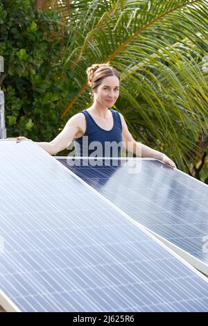 Lächelnde Frau, die hinter Solarzellen unter Palmen steht Stockfoto