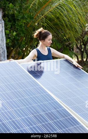 Frau, die hinter Sonnenkollektoren unter Palmen steht Stockfoto