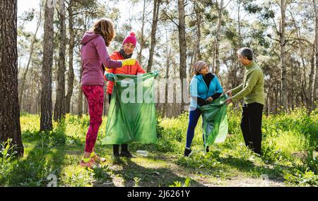 Reife Männer und Frauen sammeln Abfall in Mülltüten im Wald Stockfoto