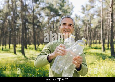 Glücklicher reifer Mann mit Plastikflaschen, die im Wald stehen Stockfoto