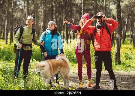 Mann, der durch ein Fernglas schaut und von Freunden und Hund im Wald steht Stockfoto