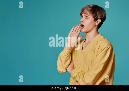 Kerl in gelben Pullover hält die Hand an den Mund rufen Sie jemanden Stockfoto