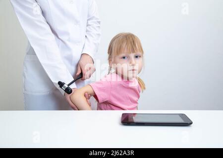 Der Arzt untersucht den Trizeps-Reflex bei einem Mädchen im Alter von 5 Jahren. Untersuchung durch einen Neurologen im Büro, medizinisches, Nervensystem. Stockfoto