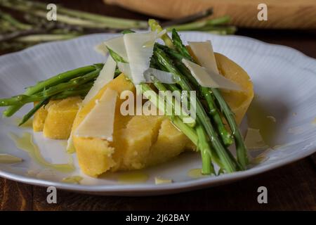 Gerollter Maisbrei mit Spargel und Käseflocken auf weißem Teller und dunklem Holzhintergrund Stockfoto