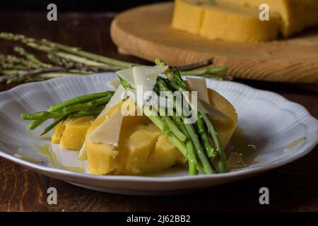 Gerollter Maisbrei mit Spargel und Käseflocken auf weißem Teller und dunklem Holzhintergrund Stockfoto