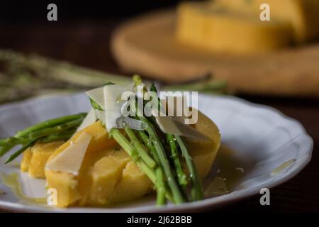 Gerollter Maisbrei mit Spargel und Käseflocken auf weißem Teller und dunklem Holzhintergrund Stockfoto