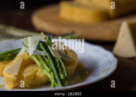 Gerollter Maisbrei mit Spargel und Käseflocken auf weißem Teller und dunklem Holzhintergrund Stockfoto