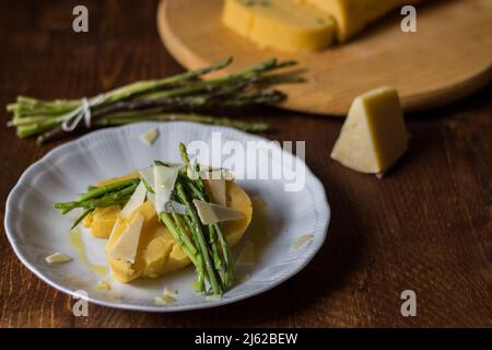 Gerollter Maisbrei mit Spargel und Käseflocken auf weißem Teller und dunklem Holzhintergrund Stockfoto